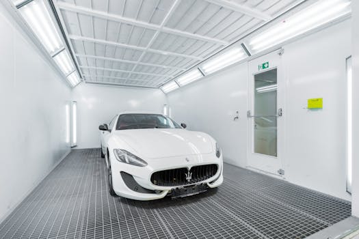 White luxury car inside a well-lit paint booth, showcasing sleek design and sophistication.